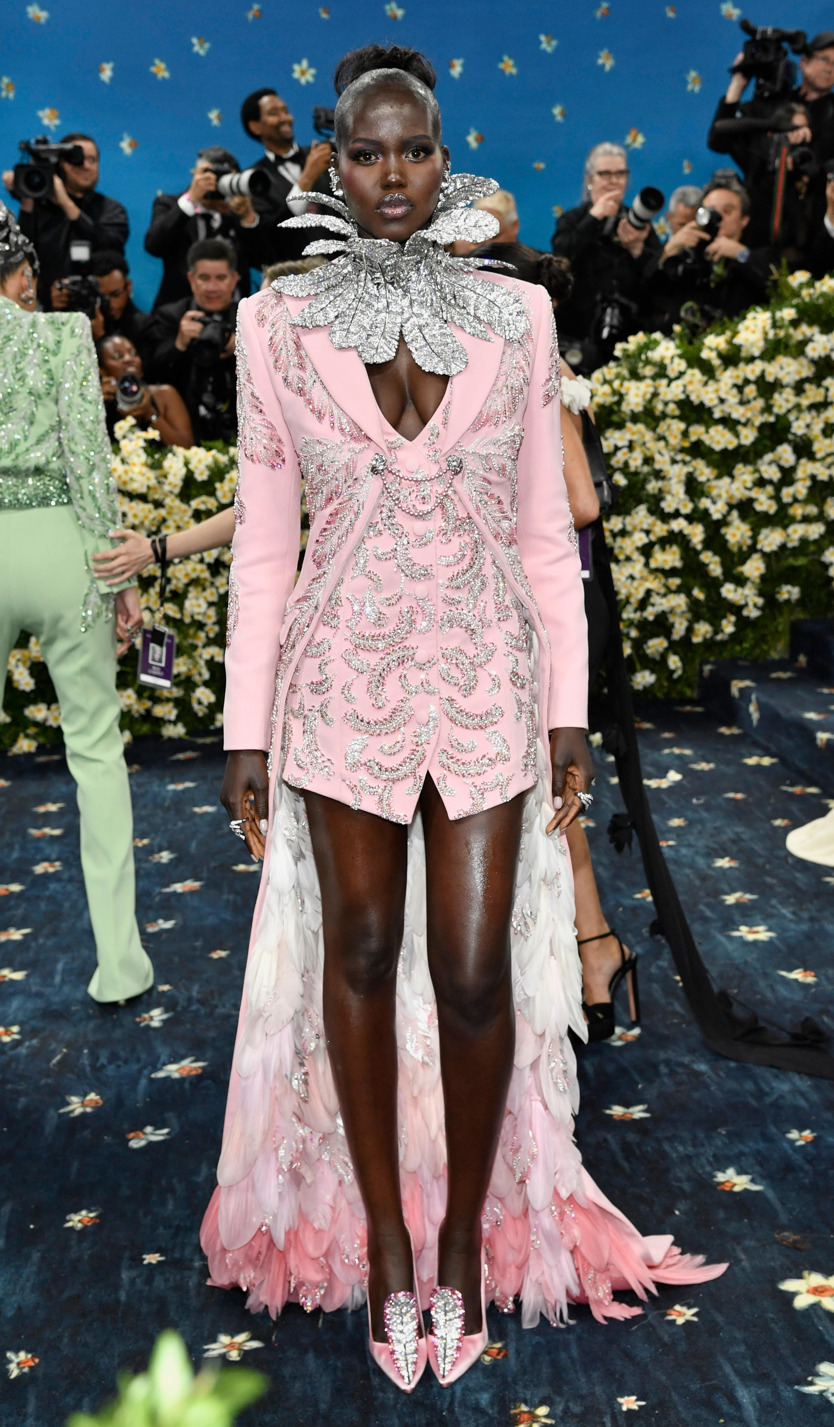 Adut Akech wearing a pale pink blazer with a pink feathery train and a silver feather collar