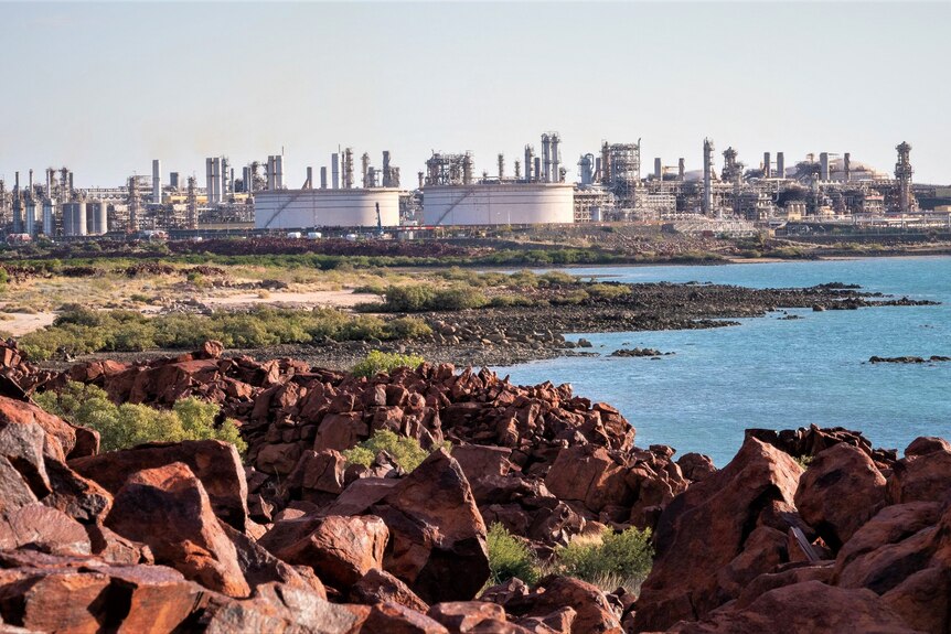 A large gas plant on the edge of a bay, with red rocks in the foreground