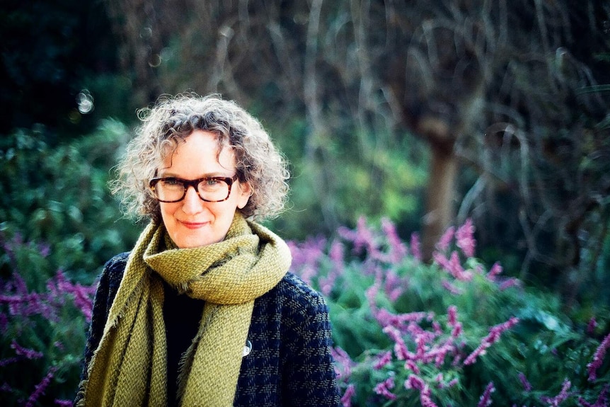 Middle-aged woman with blonde curly hair stands in front of a garden with lavender.