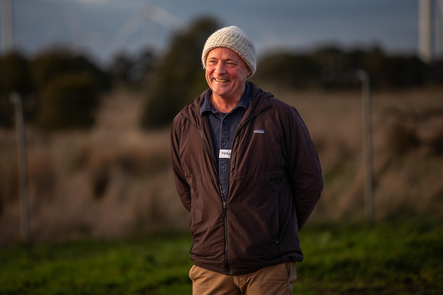 smiling man in beanie stands in grassy wildlife sanctuary