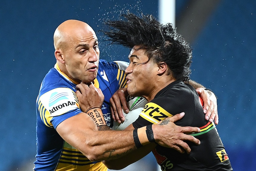 A Parramatta NRL player holds a Penrith opponent around his upper body as he attempts a tackle.