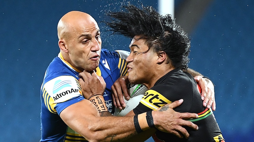 A Parramatta NRL player holds a Penrith opponent around his upper body as he attempts a tackle.