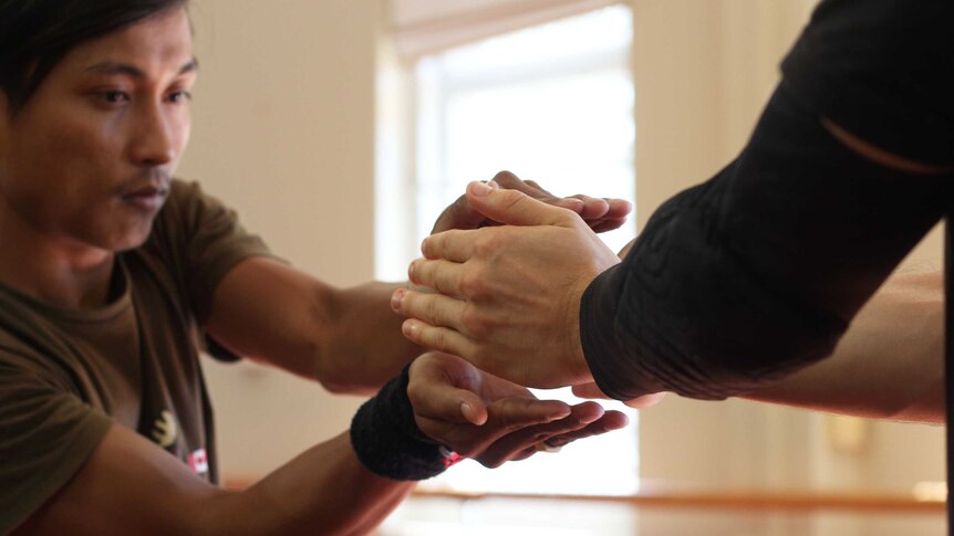 A man reaches for another man's hands.