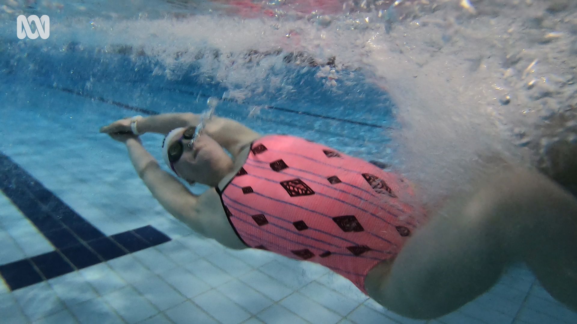 a female swimmer underwater in pink and black simmers pushing off the wall