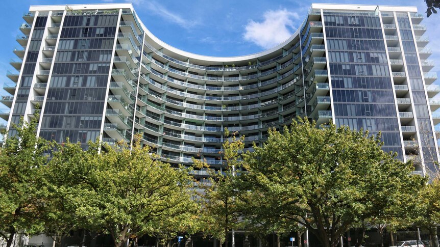 A curved, tall apartment building in Canberra with trees in the foreground.