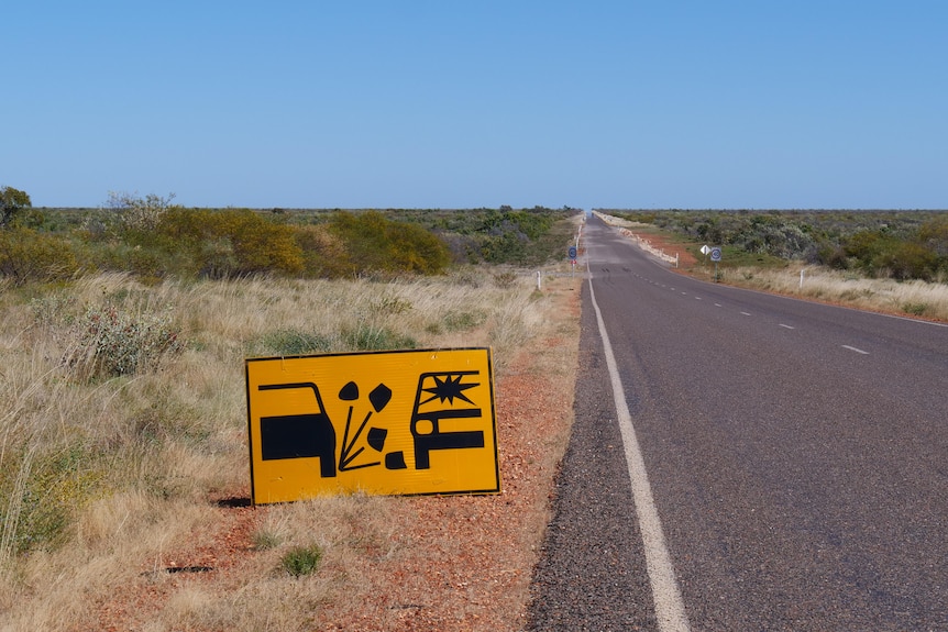 A yellow warning sign on the side of a sealed road indicated rocks may fling up at passing traffic.