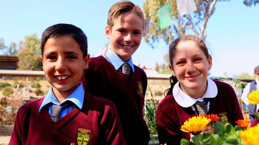 Three students with a flower bed in the St. Raphael's garden