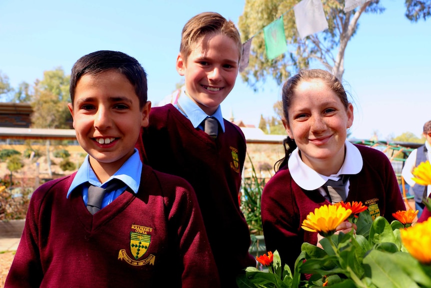 Three students with a flower bed in the St. Raphael's garden.