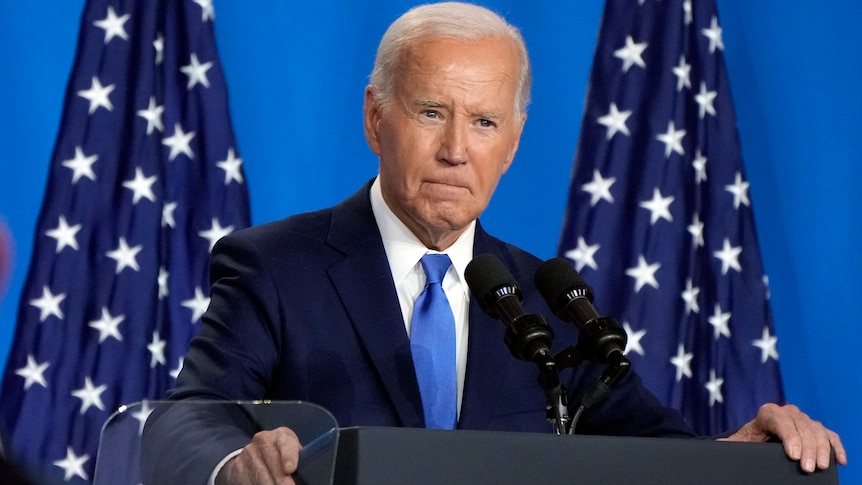 Joe Biden speaks at a news conference in front of two US flags.