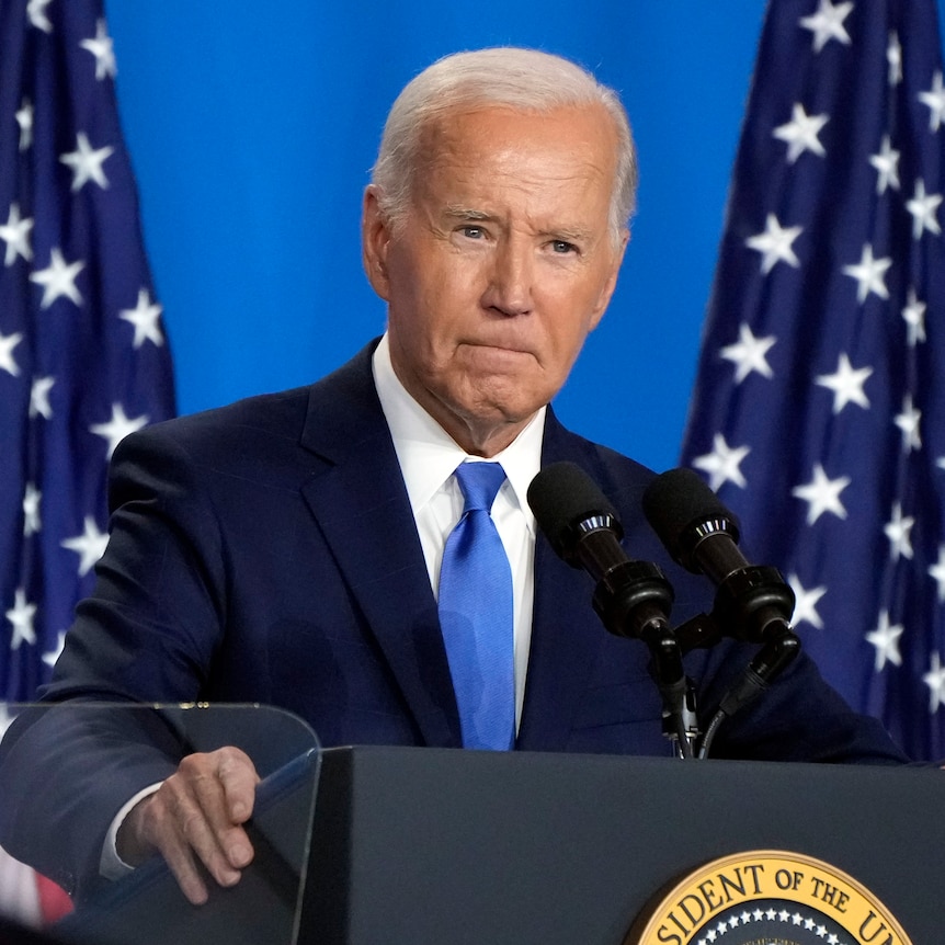 Joe Biden speaks at a news conference in front of two US flags.