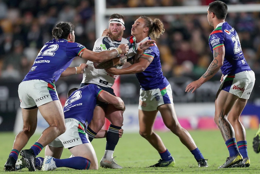 Josh McGuire stands surrounded by four Warriors players, one of whom is tackling his legs while two others grab his upper body.
