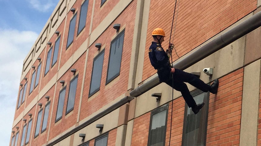 Commissioner Darren Hine abseils down the Police Headquarters in Hobart.