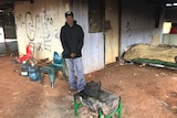 Dion Williams stands outside his tinshed home, with a teapot over the fire.