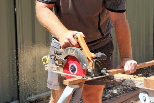 An unidentified tradie cuts a piece of wood.