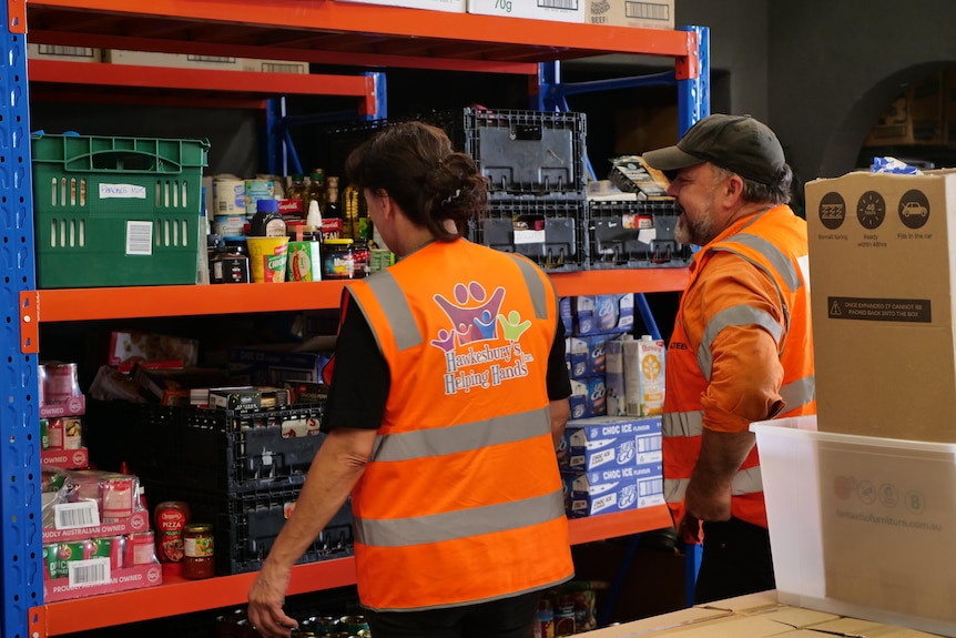 A man and a woman wearing orange vests examine a shelf of tinned food