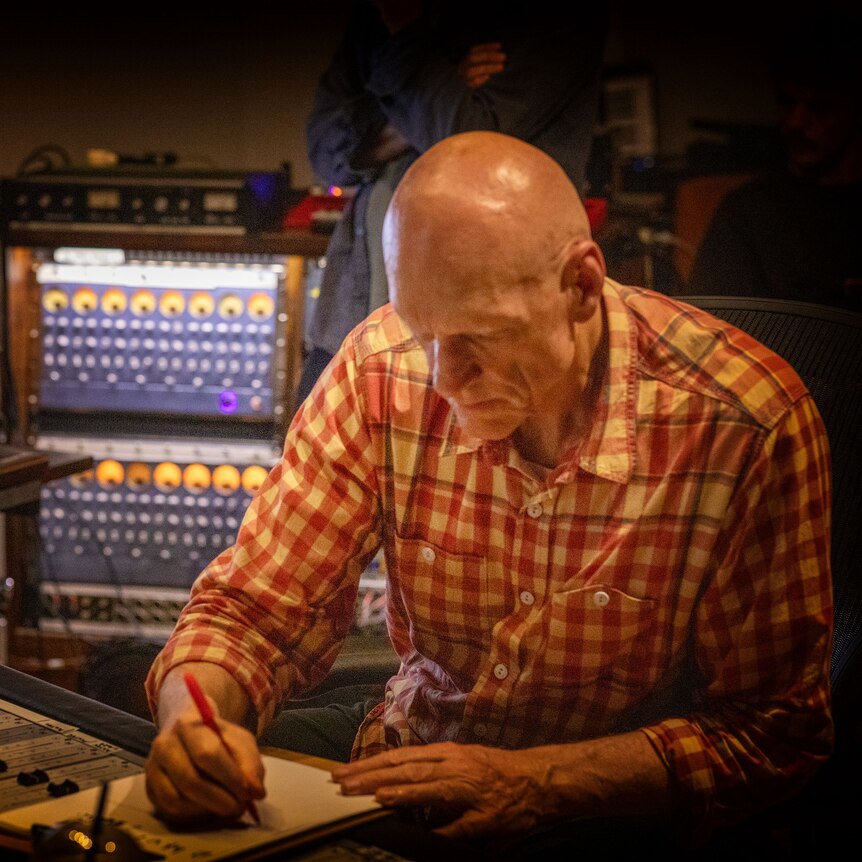 Peter Garrett sits in music studio seated at table writing in a notebook, his head down