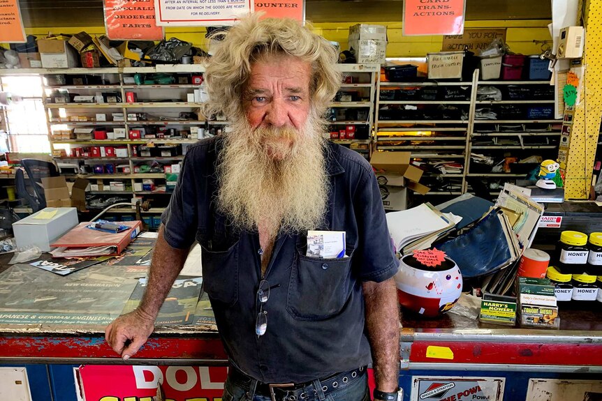 Man leans on counter in mower shop.