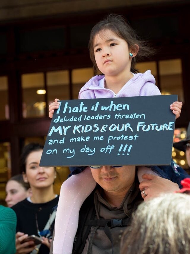 A young child holds  a sign as she sits on her father's shoulders.
