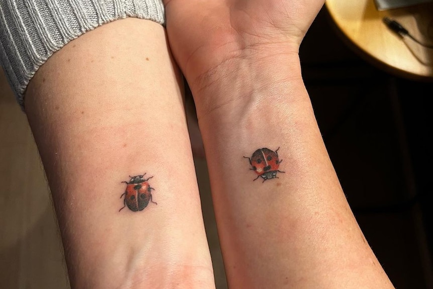 Jonassen and her sister hold out their arms side by side to show their red and black ladybug tattoos