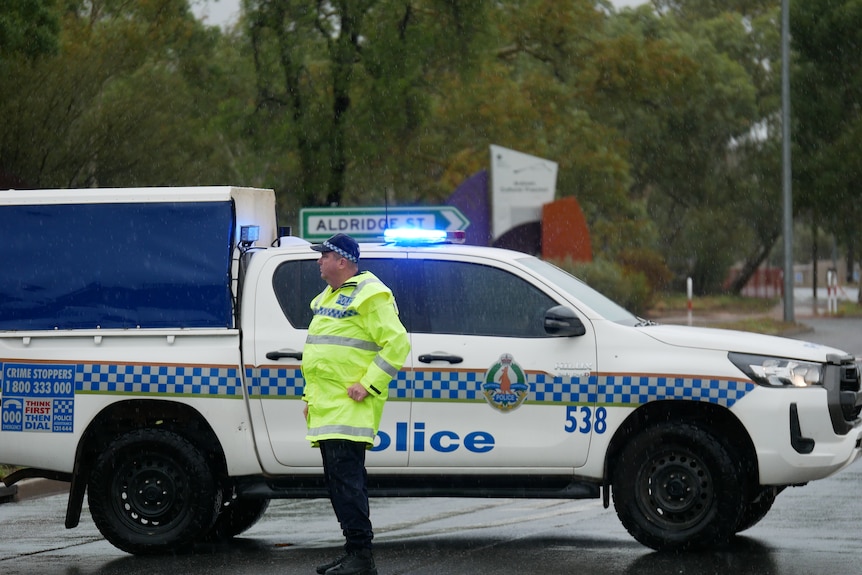 A police man standing in high-vis next to a police wagon, parked across a road