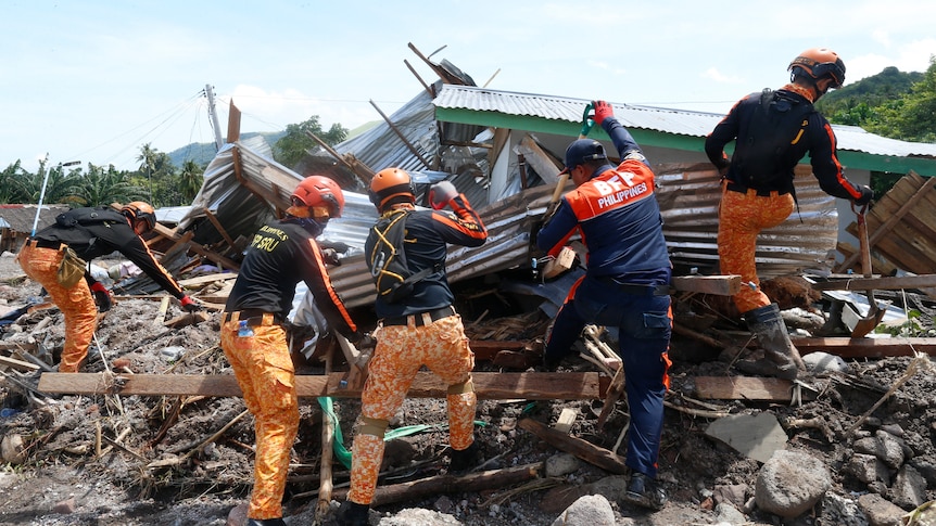 Rescuers dressed in range pants dig through the debris of a damaged house. 