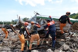 Rescuers dressed in range pants dig through the debris of a damaged house. 