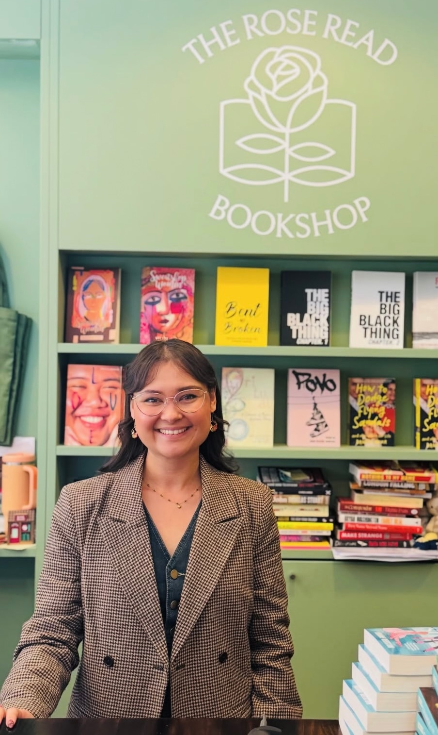 Mischa Parkee standing in front of a bookshelf, smiling, reading glasses, suit jacket