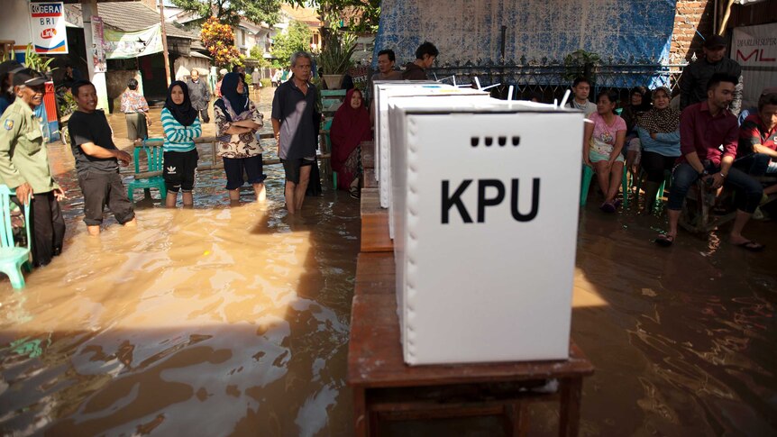People queue up to vote at a polling station inundated by flood waters as tables carrying polling boxes rise above the water.