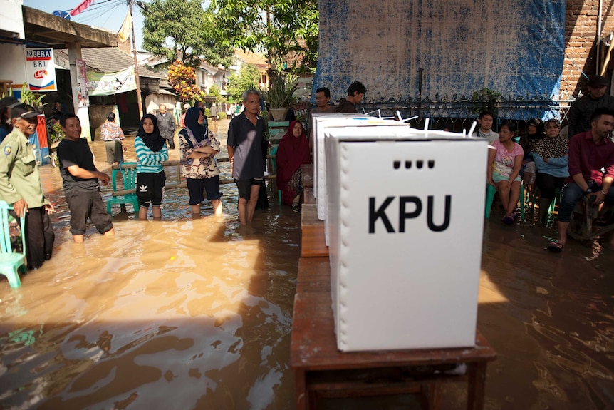 People queue up to vote at a polling station inundated by flood waters as tables carrying polling boxes rise above the water.
