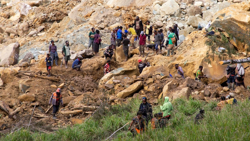 Dozens of people stand on large rocks and soil searching for survivors after a landslide