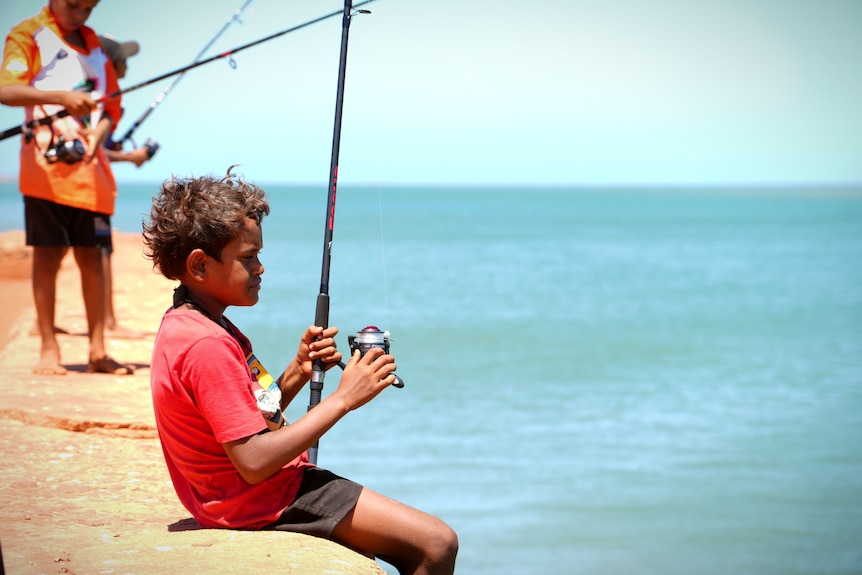 A boy in a red shirt  reels in a fish