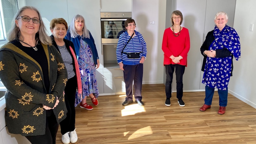 Group of older women standing in an empty kitchen.