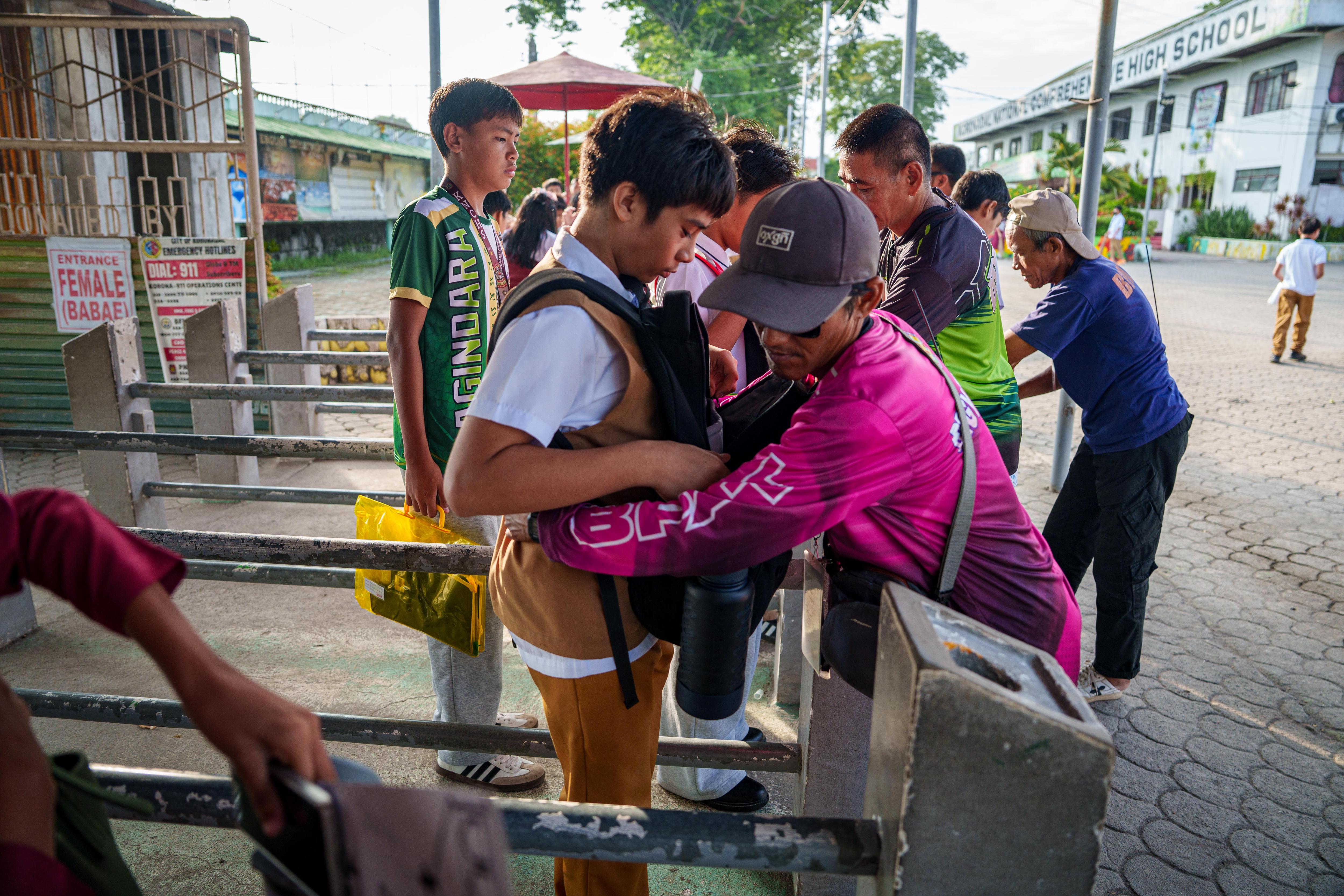 A schoolboy is being patted down by a security guard before entering the school gates.