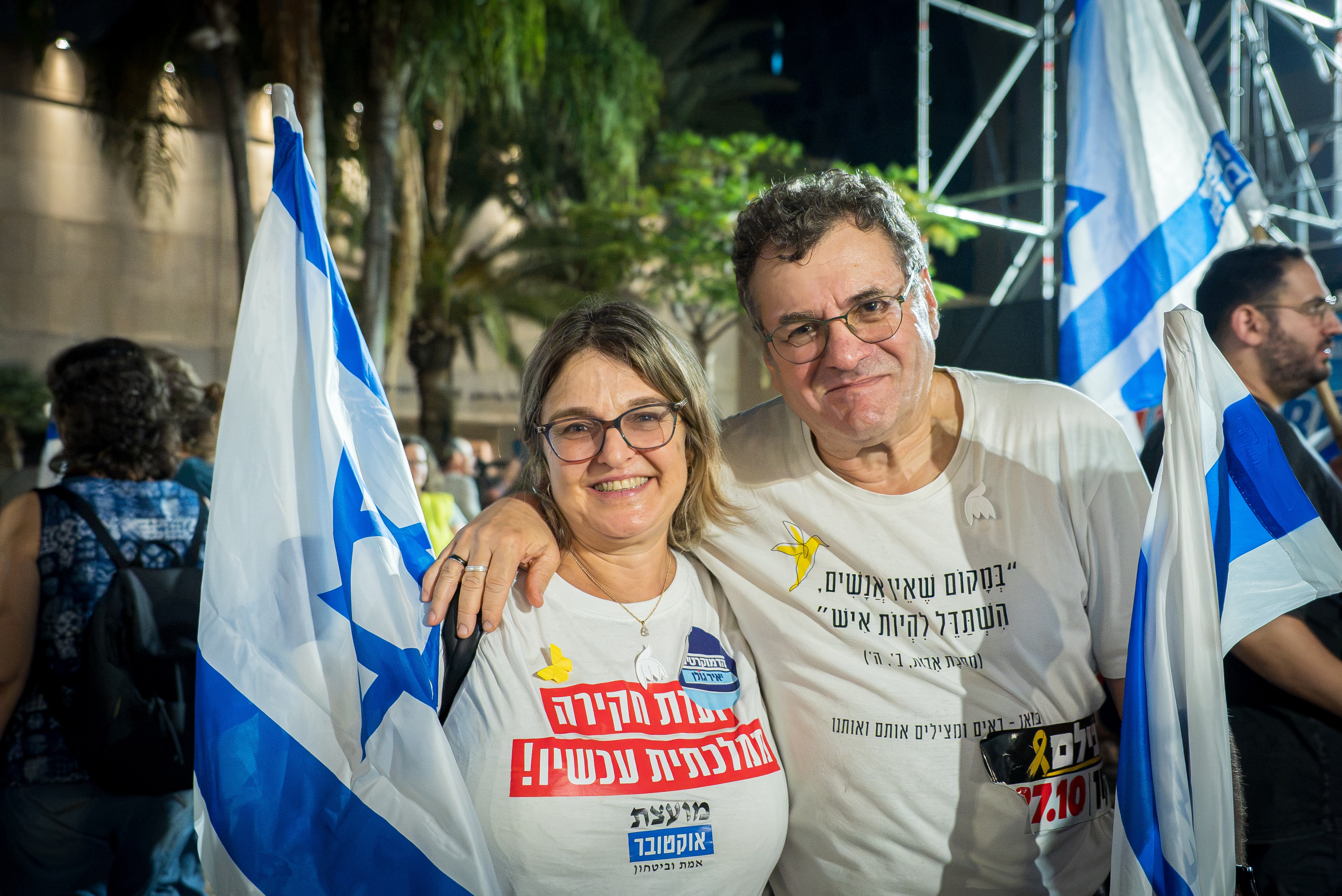 A man (right) and a woman, in slogan teeshirts, speak to the ABC holding blue and white flags.