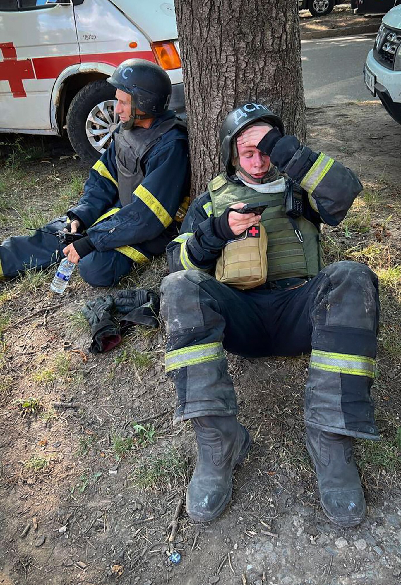 Emergency services workers sit on the ground and drink water. 