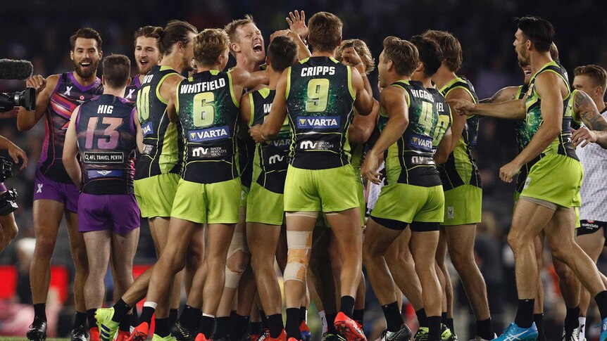 AFLX players celebrate in a group on the ground before the kickoff at Docklands.