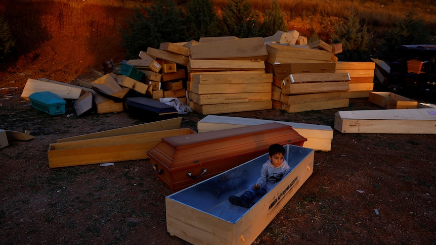 A boy sits inside an open coffin. 