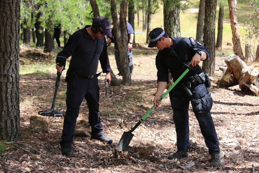 Police with shovels and other tools search a forest.