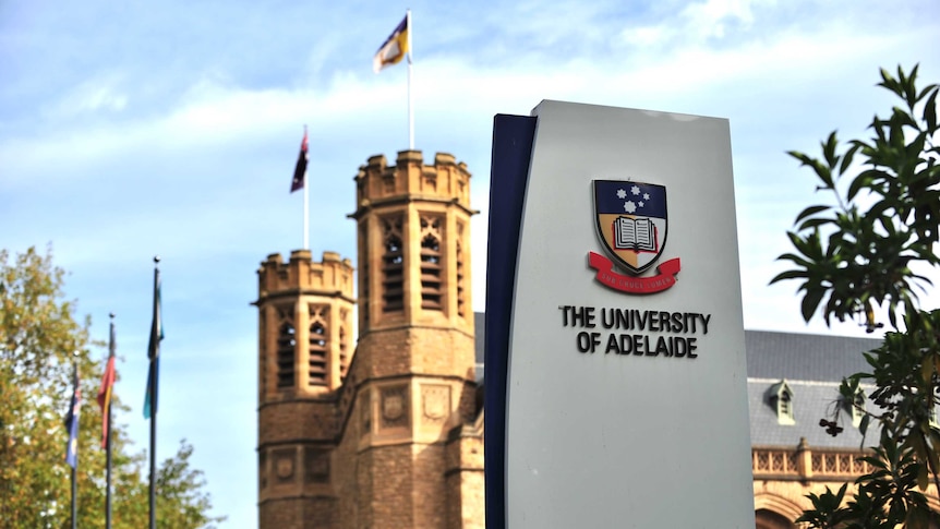 A modern University of Adelaide sign with a 19th century sandstone building behind