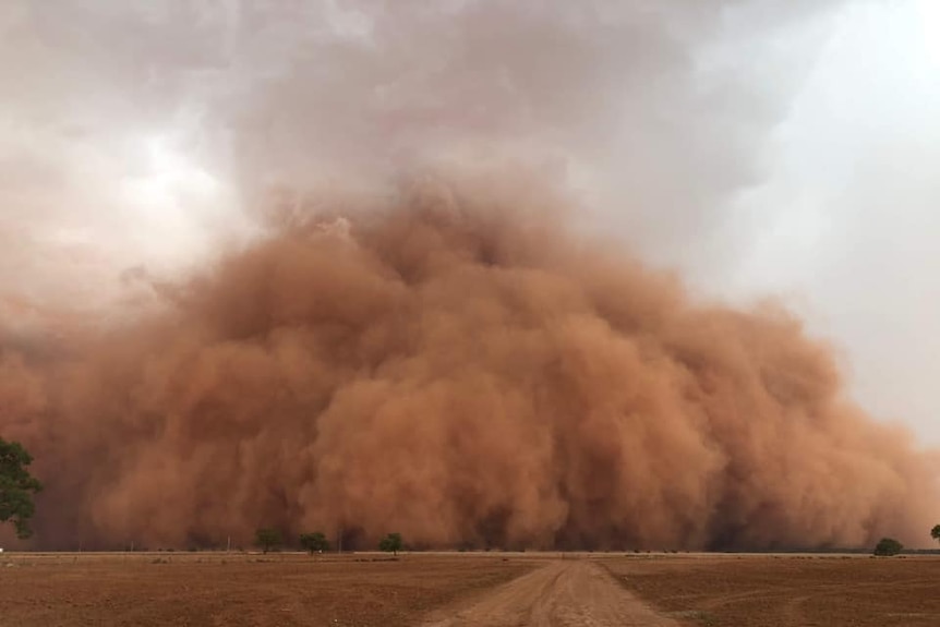 A large red cloud of dust looms over a rural landscape.