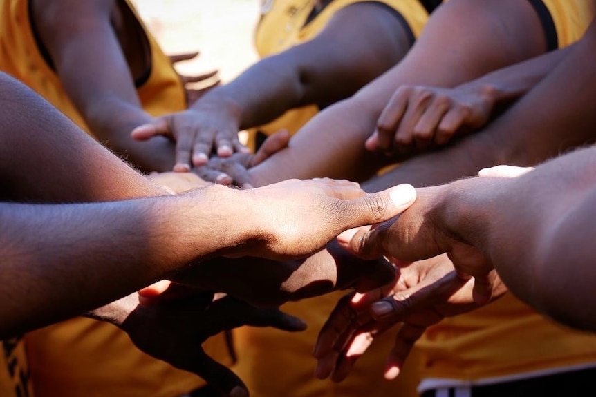 A close up of hands in a huddle at a football match in Bidyadanga June 2022