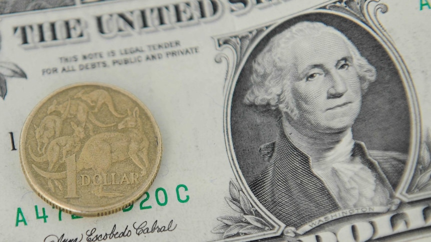 An Australian dollar coin sits on a US dollar bill