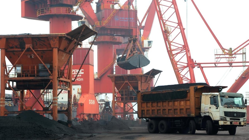 Imported coal is seen lifted by cranes from a coal cargo ship onto a truck at a port in China