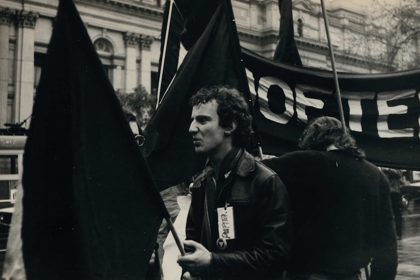 Gay Pride Week march in 1973 in Melbourne with one man in the foreground carrying a flag.