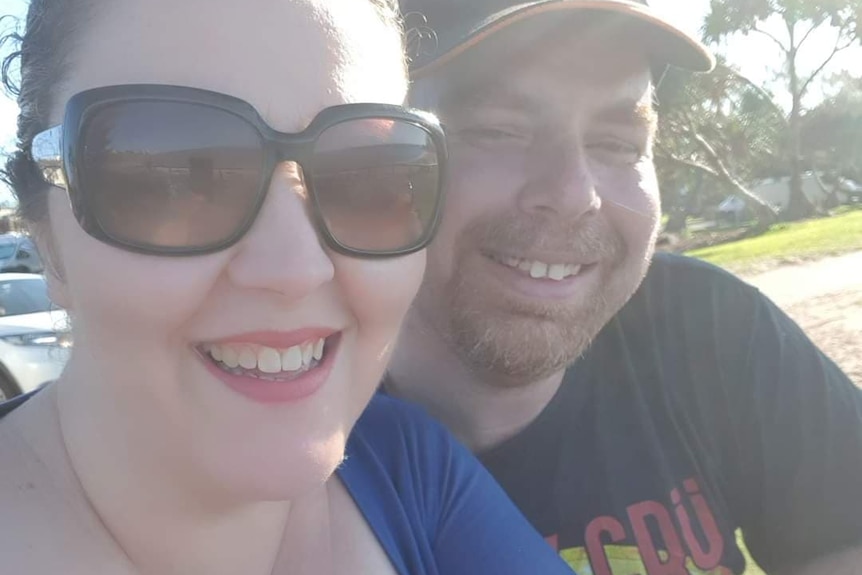 Photo of Anthony Ridley, a man with a beard wearing a hat, and his wife, sitting in a sunny park.