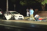 Plain-clothed police examine the contents of a damaged white BMW on the side of the road.
