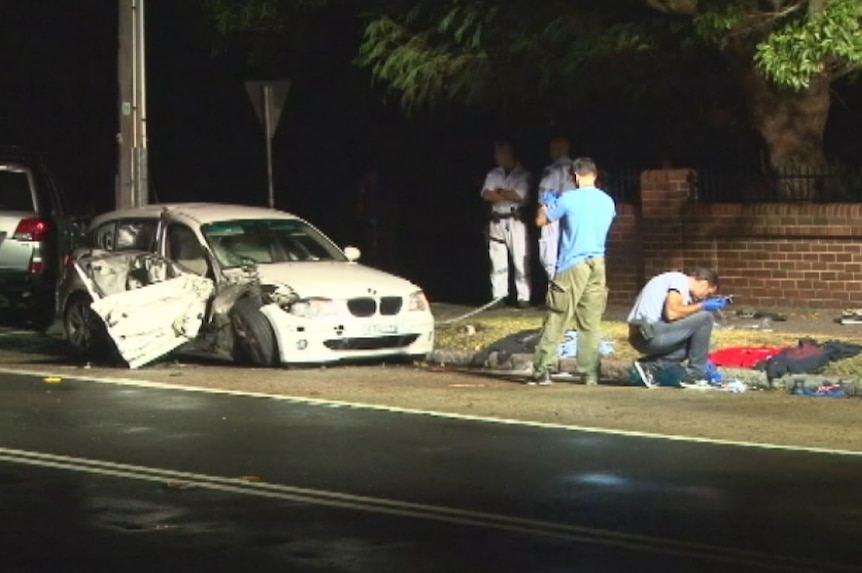 Plain-clothed police examine the contents of a damaged white BMW on the side of the road.