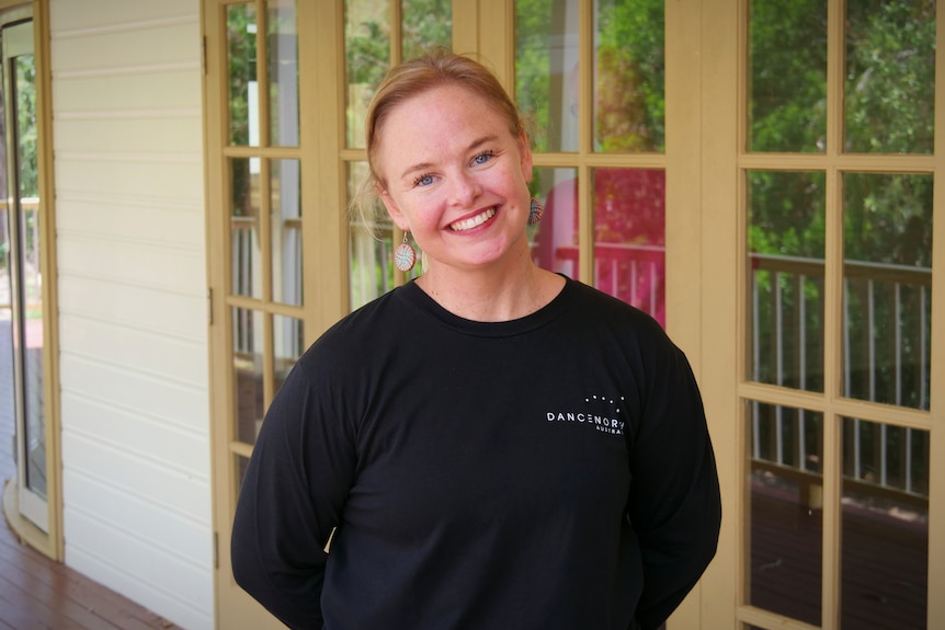 A woman smiling in front of the windows of a community hall