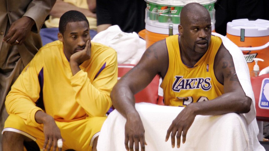 Kobe Bryant sits with his hand on his face, looking down. Shaq sits next to him, looking in the other direction.