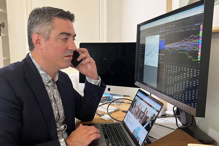 A man speaks on his phone while looking at his computer. He's wearing a suit.